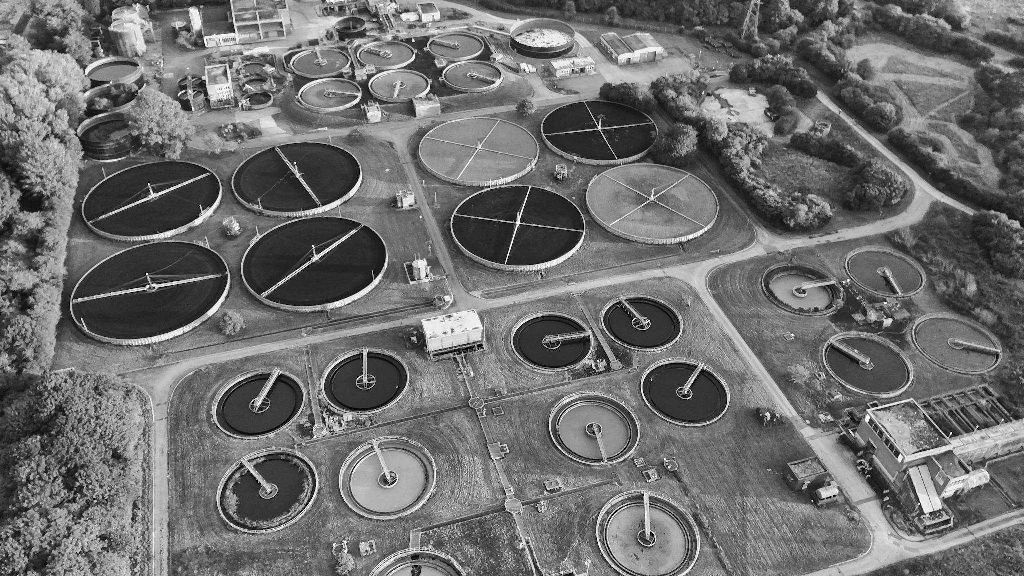 Black and white aerial view of a wastewater treatment plant in the English countryside.