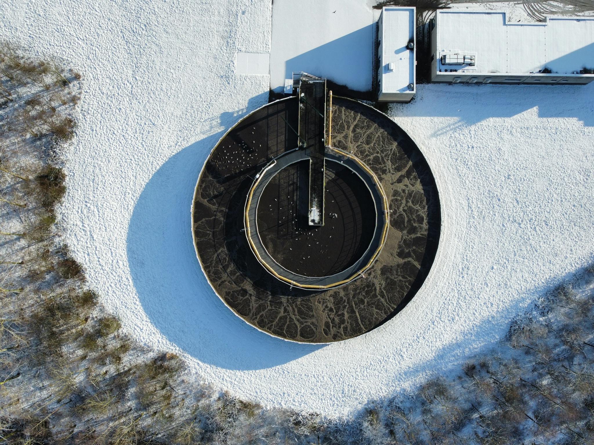 Drone shot of a circular wastewater treatment plant surrounded by winter snow.